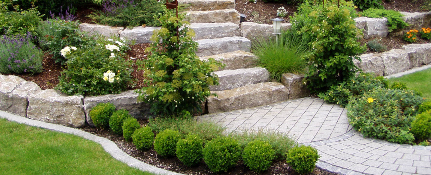 Gartentreppe aus Naturstein mit Böschungssteinen zur Terrassierung und üppiger Bepflanzung