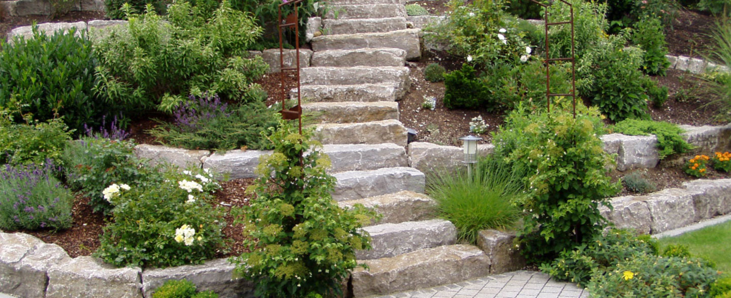 Treppe aus Naturstein-Blockstufen für den Außenbereich mit einem großen Garten und am Hang angelegten Blumenbeeten