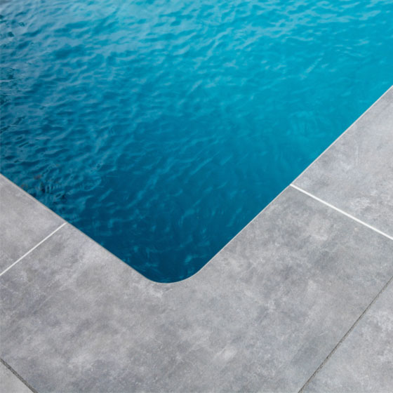 Swimmingpool mit gerundete Ecken und grauen Terrassenplatten drum herum
