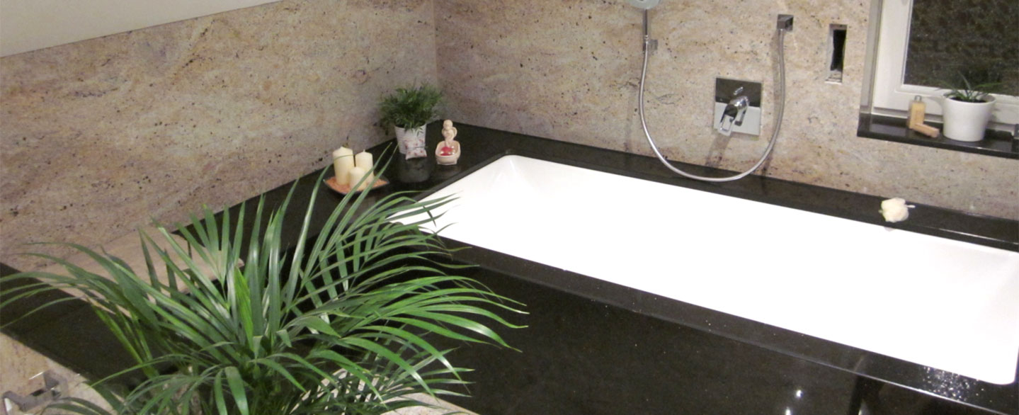 Badezimmer mit dunkler Badewannenverkleidung und heller Wandverkleidung aus Naturstein