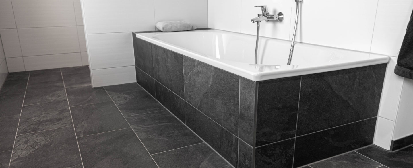 Verlegtes Badezimmer aus dunkelgrauen Schieferfliesen und einer Badewanne mit Verkleidung