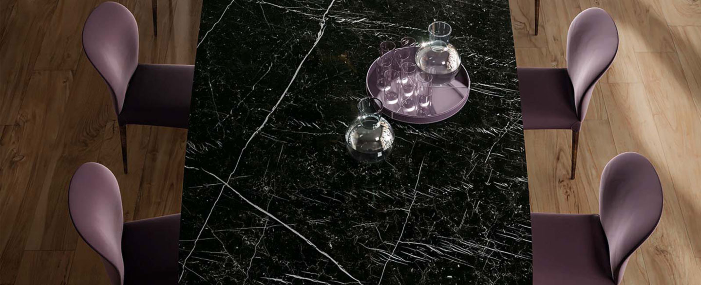 angeschnittene Ansicht eines Tisches aus schwarzer Marmoroptik auf dem ein violettes Tablet mit Wassergläsern steht und violetten Stühlen