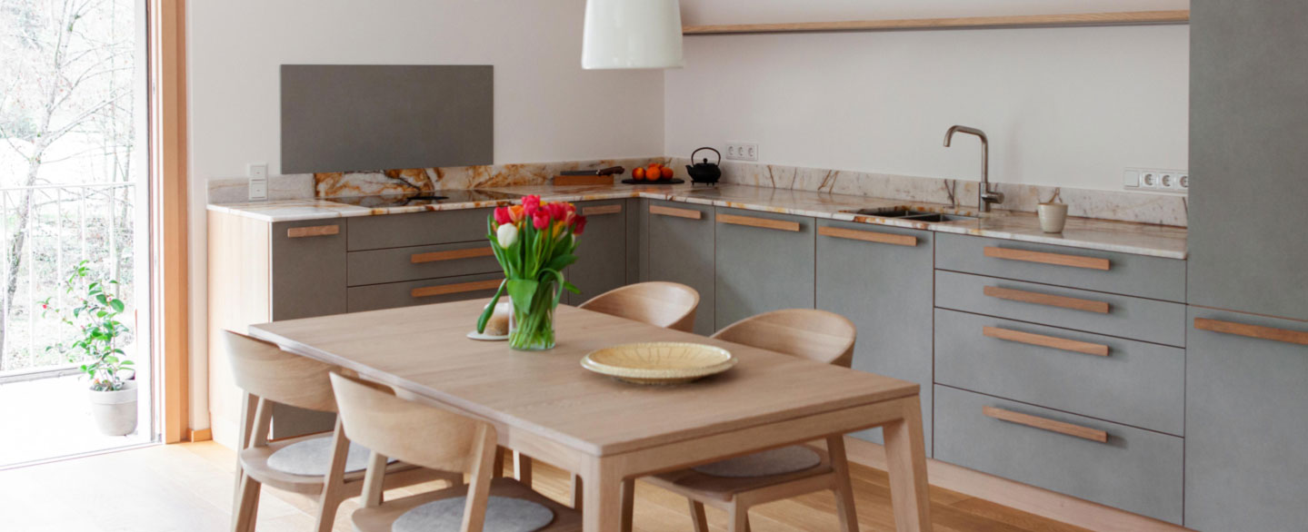 helle Küche mit Esstisch aus Holz, grauen Küchenfronten und Arbeitsplatte aus Naturstein Samba Sunset