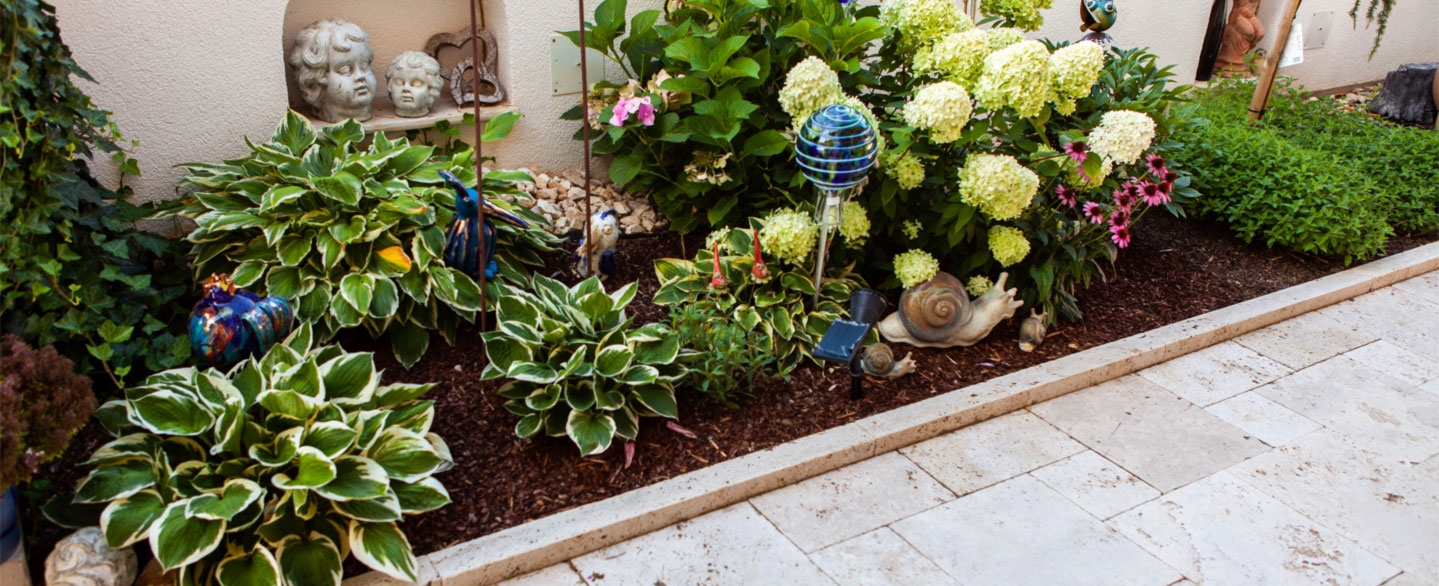 üppiges Blumenbeet mit Hortensien eingefasst von Travertin Ransenkanten und Terrassenplatten im römischen Verband