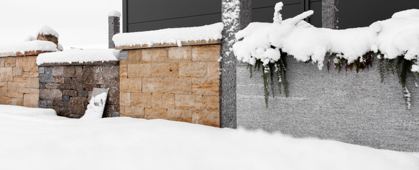 verschiedene Mauern aus Naturstein in der Ausstellung bei Dnger Stone unter einer Schneedecke