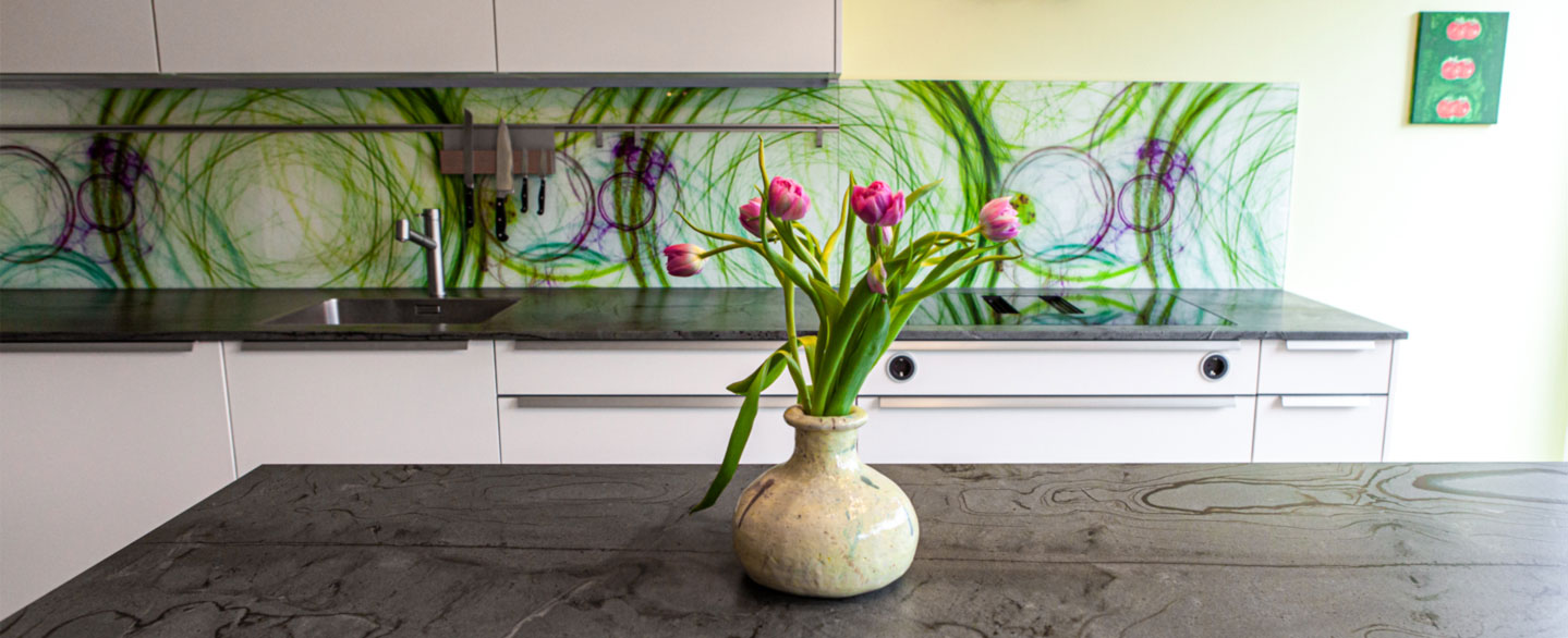 Vase mit rosa Tulpen auf einer Natursteinarbeitsplatte und bunte Glasrückwand im Hintergrund