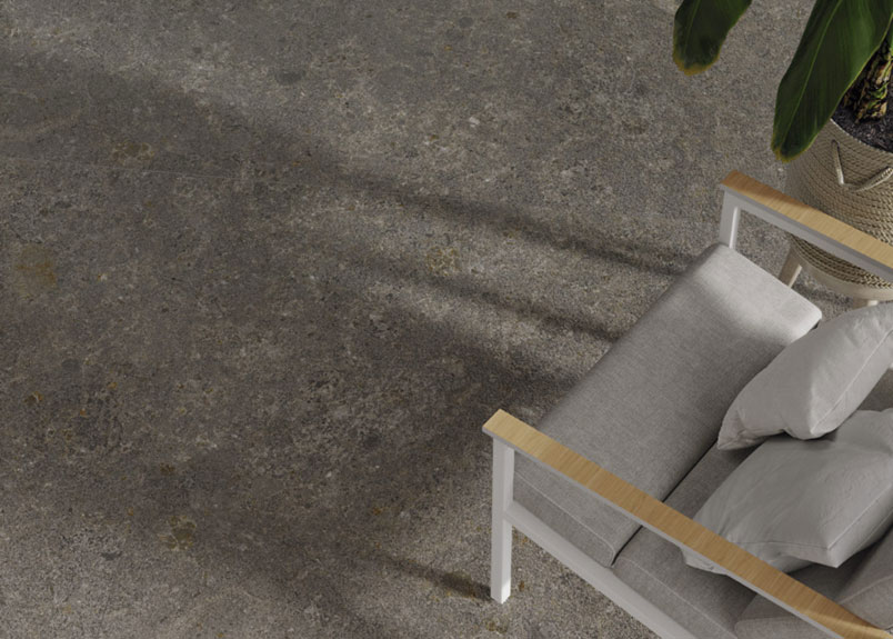 Keramik Bodenplatte "Moonlight Grey" mit einem Stuhl und einer grünen Pflanze daneben