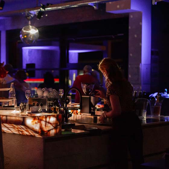 discokugel-cafémaschiene-josefine-rasterbild Theke mit Siebträgermaschine- im Hintergrund tanzende Menschen und eine Discokugel.