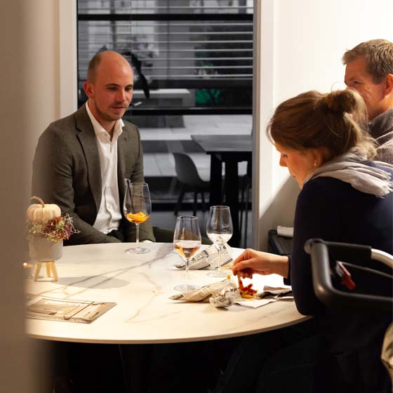 lucas-kundengespräch-tisch-rasterbild 3 Perosnen sitzen an einem Steintisch und unterhalten sich. Eine Person isst Pommes.
