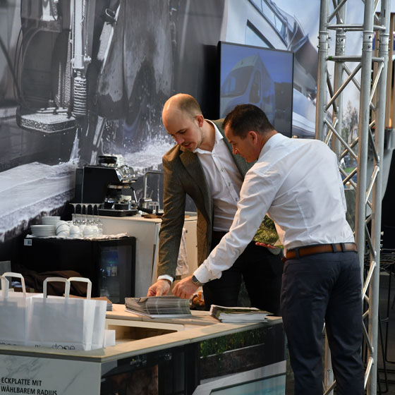 Lucas_Kundengespräch Zwei Personen im Gespräch auf einem Messestand.