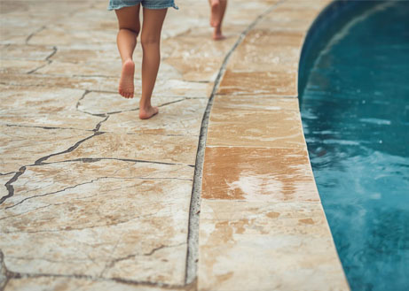 poolrandsteine-natursteinpoolumrandung-rutschhemmend-kinderrennen-poolrandplatten-travertin Kinder rennen über nasse Poolrandplatten aus Naturstein und rutschen nicht aus