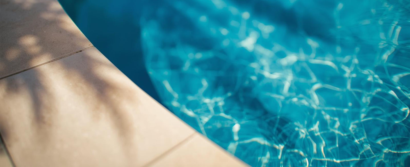 poolumrandung-feinsteinzeug-natursteinumrandung-wasser Detailaufnahme von mediterraner Poolumrandung aus Feinsteinzeug oder Naturstein